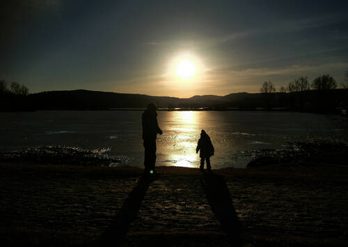 Couché de soleil sur un lac gelé. Deux enfants à contre jour le regardent.