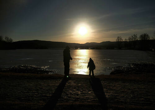 Sunset over a frozen lake. In the foreground, two children are looking at it.